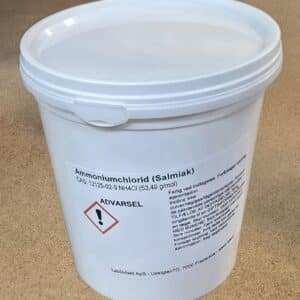 En hvid plastbeholder mærket "Ammoniumchlorid (800 g)" med advarselstekst og et faresymbol på en brun overflade.