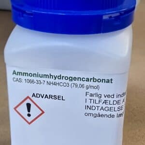 En hvid plastbeholder med blåt låg mærket Ammoniumhydrogencarbonat p.a. (500 g) og danske advarsler.