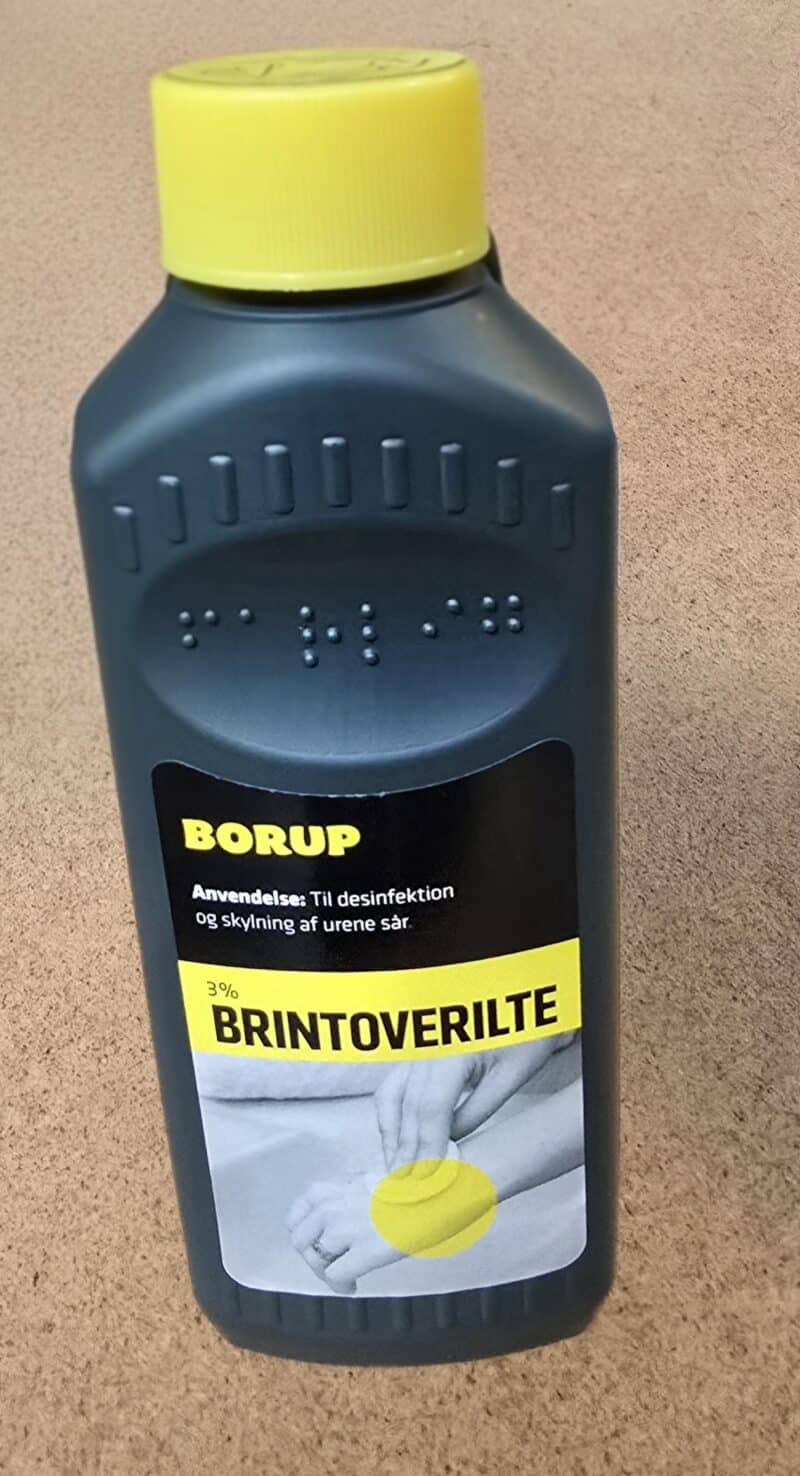 En sort flaske med Hydrogenperoxid 3% (175 ml) med en gul hætte, dansk tekst og et billede af hænder, der hælder væske på en klud.