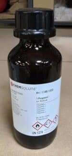 En mørk glasflaske mærket Propan-1-ol p.a. (1 liter) med faresymboler, stregkode og kemiske data på en hvid etiket.