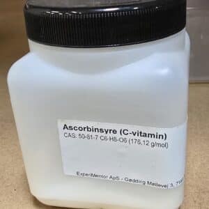 En hvid plastbeholder mærket "Ascorbinsyre, ren (200 g)" med kemiske oplysninger og virksomhedsoplysninger på en brun overflade.