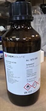 En brun glasflaske mærket 2-Methylpropan-1-ol (1 L, p.a.) med faresymboler og detaljer på en laboratorieoverflade.