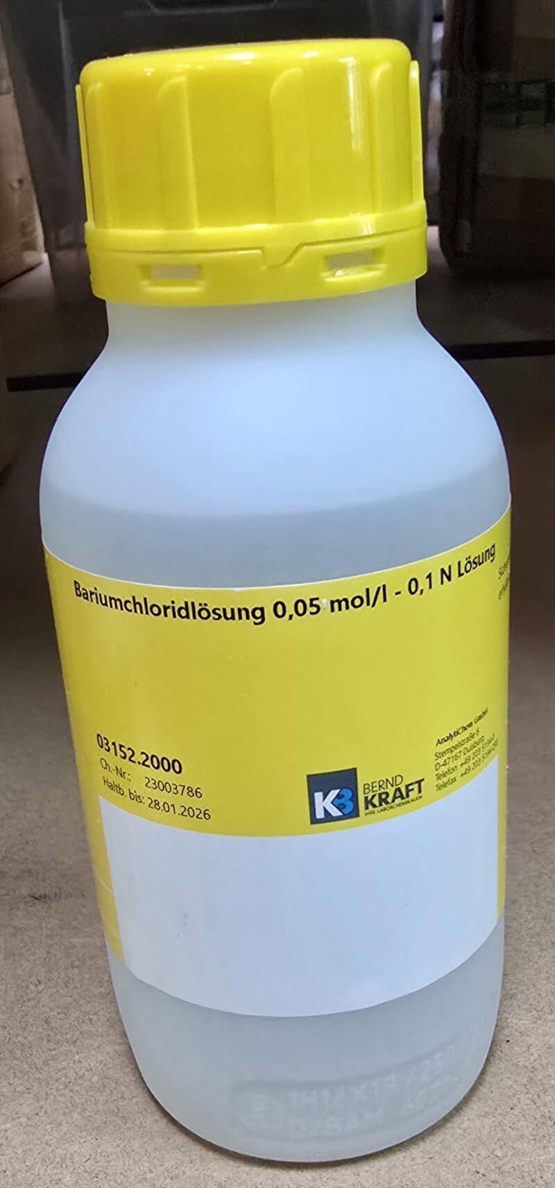 En hvid plastflaske med en gul hætte, hvorpå der står "Bariumchlorid 0,05 M (500 ml)" på tysk.