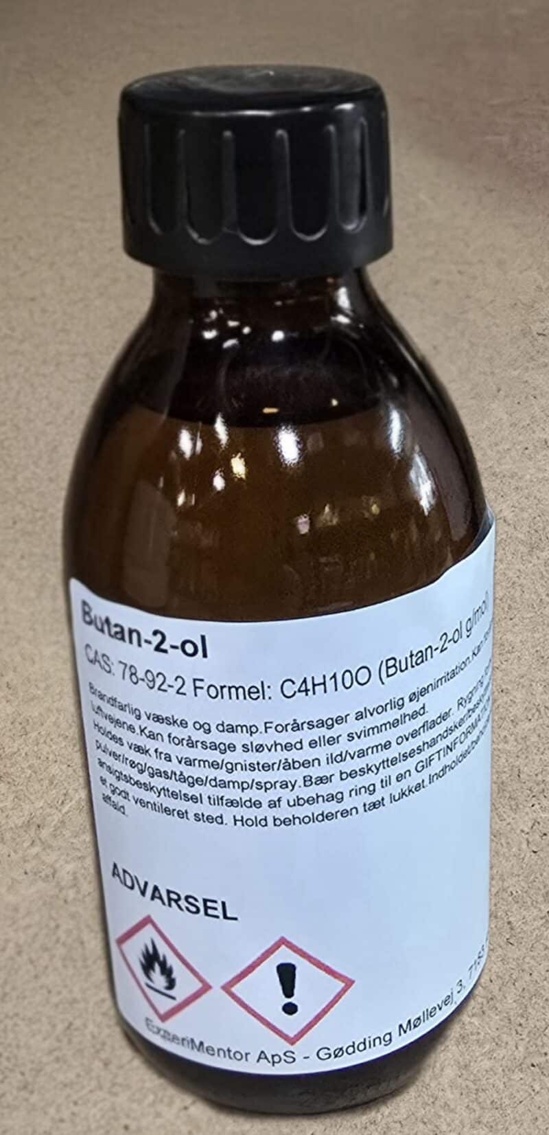 En 200 ml brun glasflaske med sort hætte, mærket Butan-2-ol og med danske advarsler og produktinformation.