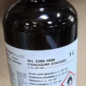 En 1-liters brun flaske mærket Eddikesyre 32% med brandfarlige og ætsende faresymboler på en beige overflade.