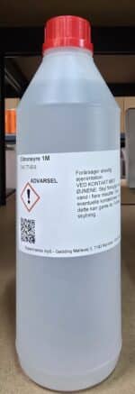 En hvid plastflaske med rød hætte mærket Citronsyre 1M (1 liter), advarsler og danske sikkerhedsanvisninger.