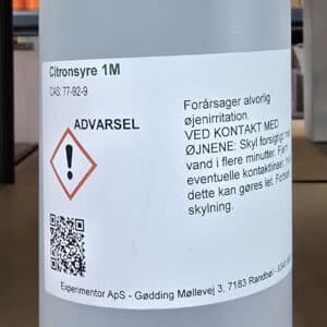 En hvid plastflaske med rød hætte mærket Citronsyre 1M (1 liter), advarsler og danske sikkerhedsanvisninger.
