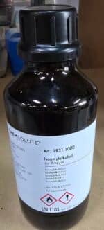 En 1-liters mørk glasflaske mærket Isoamylalkohol med faresymboler står på en laboratorieoverflade.