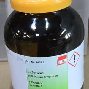 En 500 ml sort flaske med Octan-1-ol 99% med gul hætte og grøn etiket er placeret på en laboratorieoverflade.