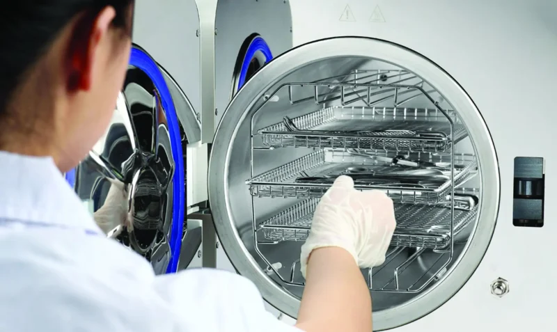 Autoclave_Toutch_Pro_CRISPIN_MED_23L_708228_2_5f86 - LabDidakt.dk Lab technician wearing gloves loading racks into an open industrial autoclave for sterilization.