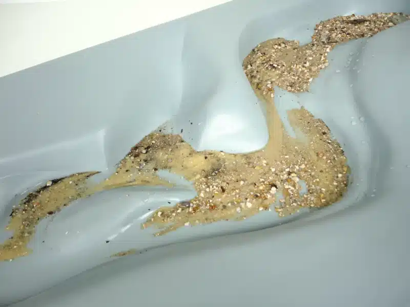 Sand og småsten spredt på den glatte, lysegrå Eksperimentel flodmodel-overflade med buede fordybninger.