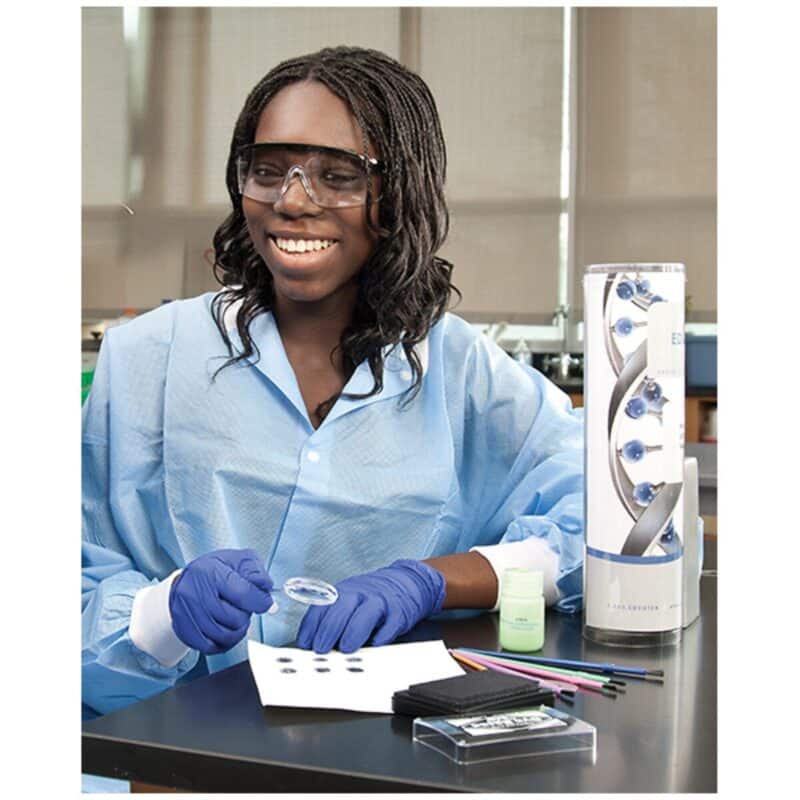 En person i kittel og handsker bruger "Kit: Hvem har efterladt fingeraftryk" til at undersøge beviser ved et laboratoriebord.