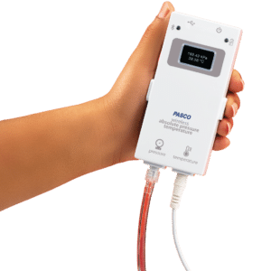 En hånd holder en PASCO trådløs absolut tryk- og temperatursensor med tilsluttede slanger og kabler.