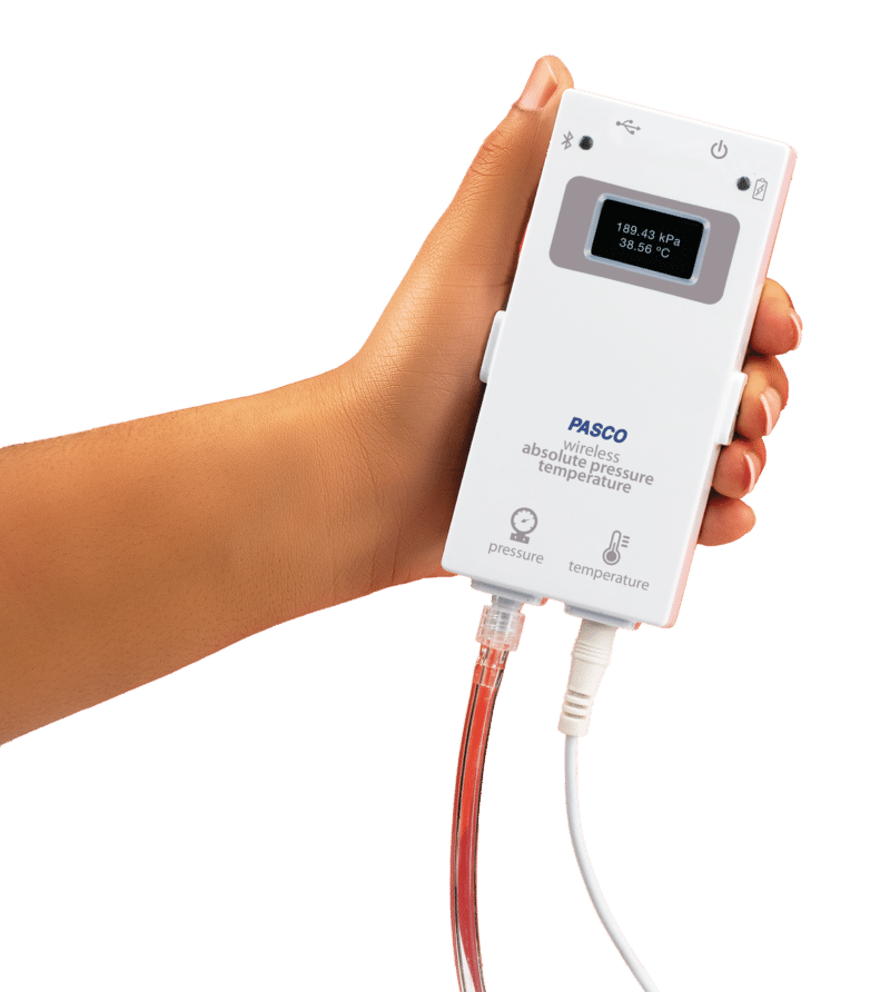En hånd holder en PASCO trådløs absolut tryk- og temperatursensor med tilsluttede slanger og kabler.