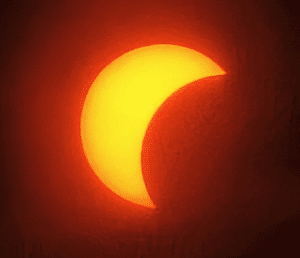 Skærmbillede 2026-08-13 144011 - LabDidakt.dk En delvis solformørkelse, hvor månen dækker en del af den strålende sol og danner en halvmåneform mod en mørk baggrund.