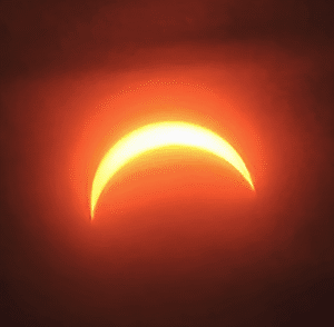 Skærmbillede 2026-08-13 144851 - LabDidakt.dk En lys, halvmåneformet delvis solformørkelse lyser orange mod den mørke himmel.